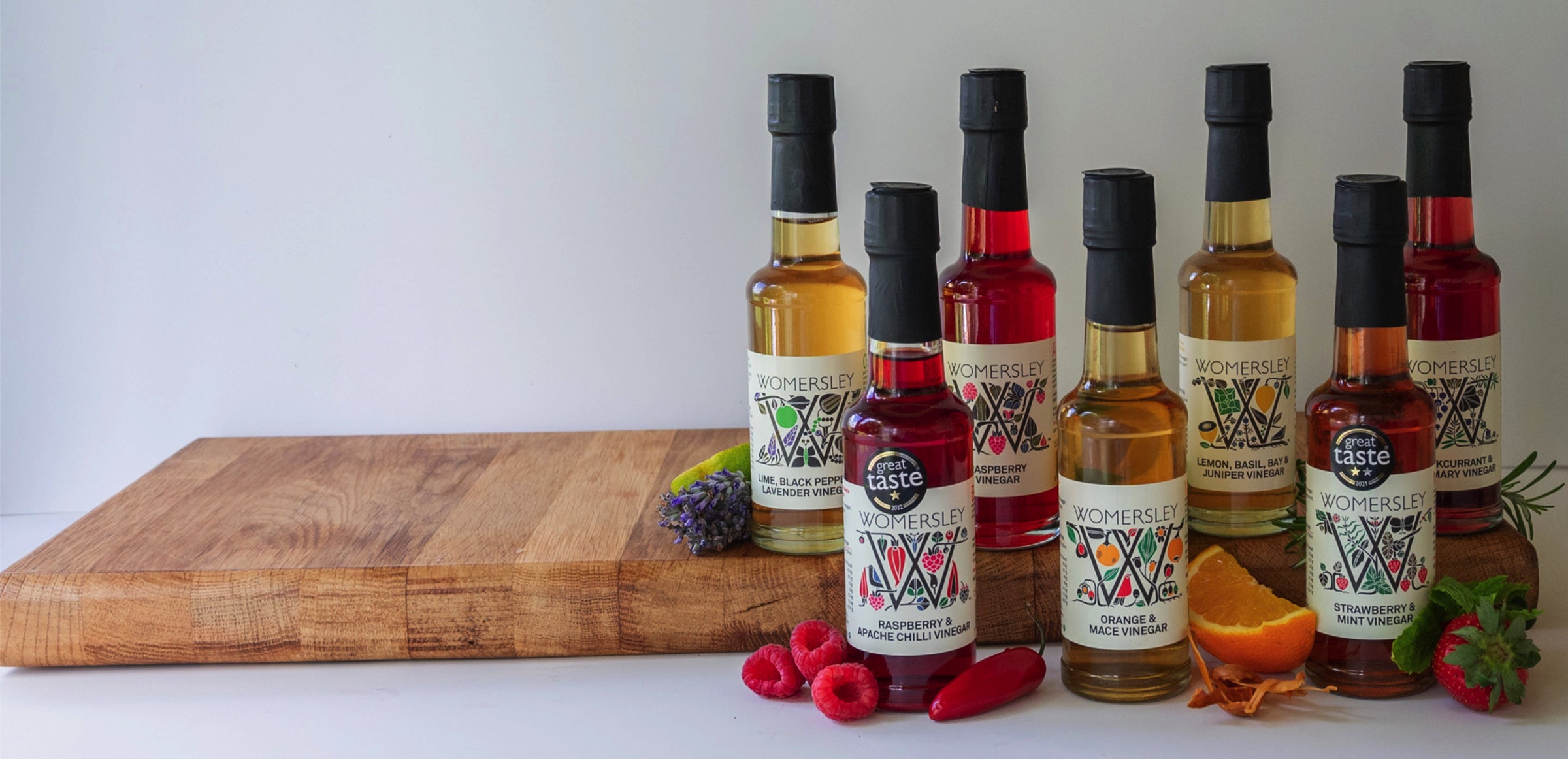 Womersley Foods Fruit Vinegar Range with Ingredients on a White Background sitting on top of a kitchen cutting board.. 