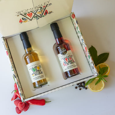 Womersley Foods Fruit & Herb vinegar opened Gift Box Enduringly Popular Vinegars with ingredients. Featuring 150ml Raspberry and Apache Chili fruit vinegar and Lemon, basil, Bay and Juniper fruit vinegar lying in the box with images of raspberry, lemon, basil, bay and Apache chili on a white background.